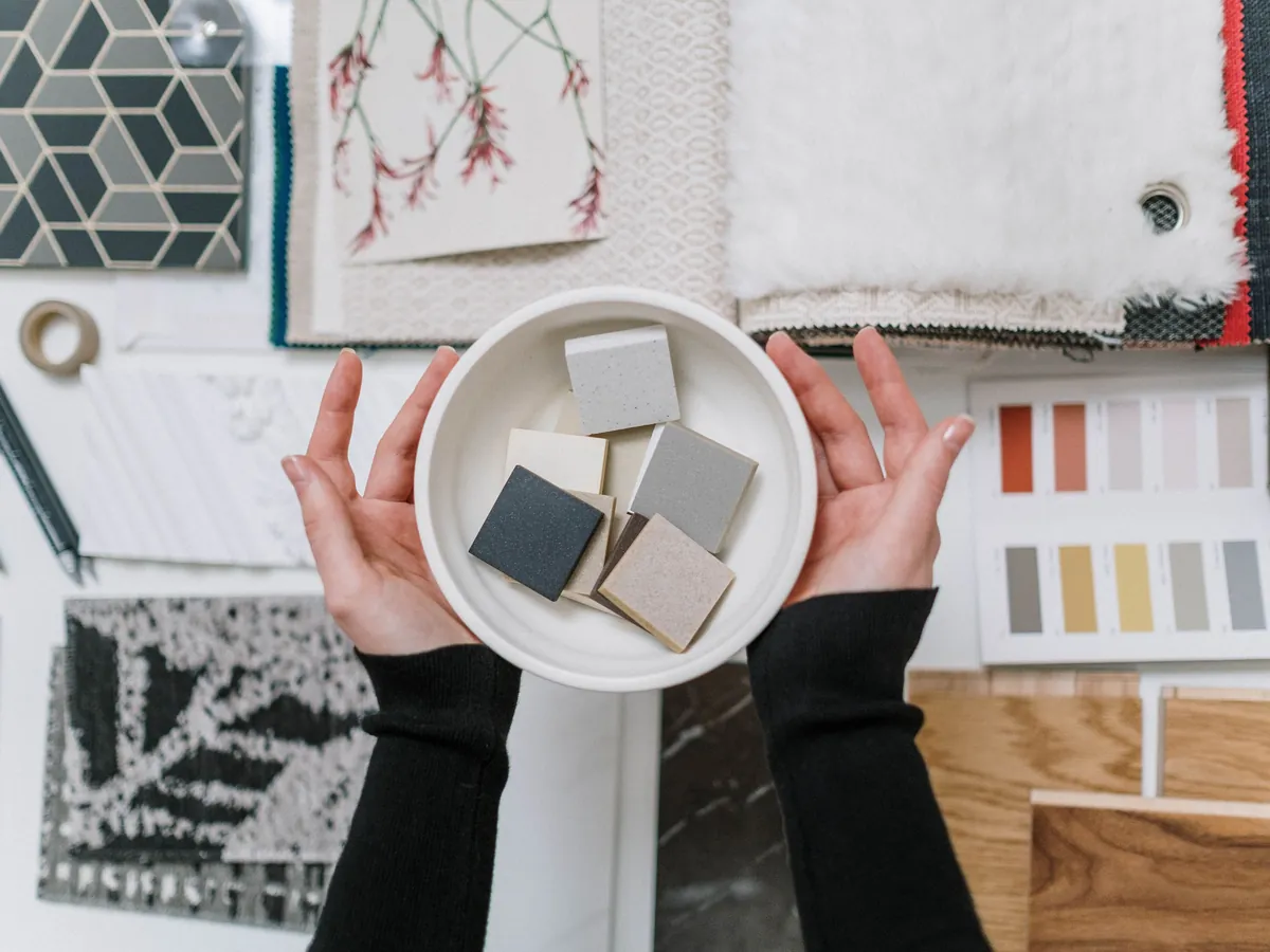 Hands holding stone samples over a moodboard of tiles, fabrics and paint swatches